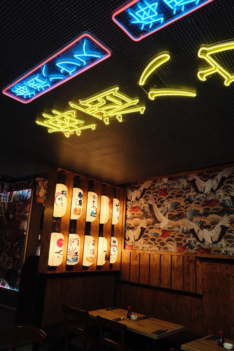 Dining room with neon lettering on the ceiling, a wall of lanterns and wallpaper with cranes